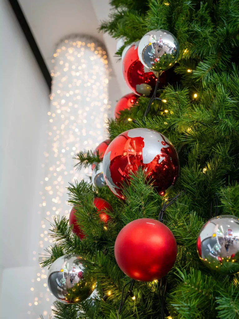 Kerstboom versierd met rode en zilveren ballen en warm witte verlichting tegen een witte achtergrond.