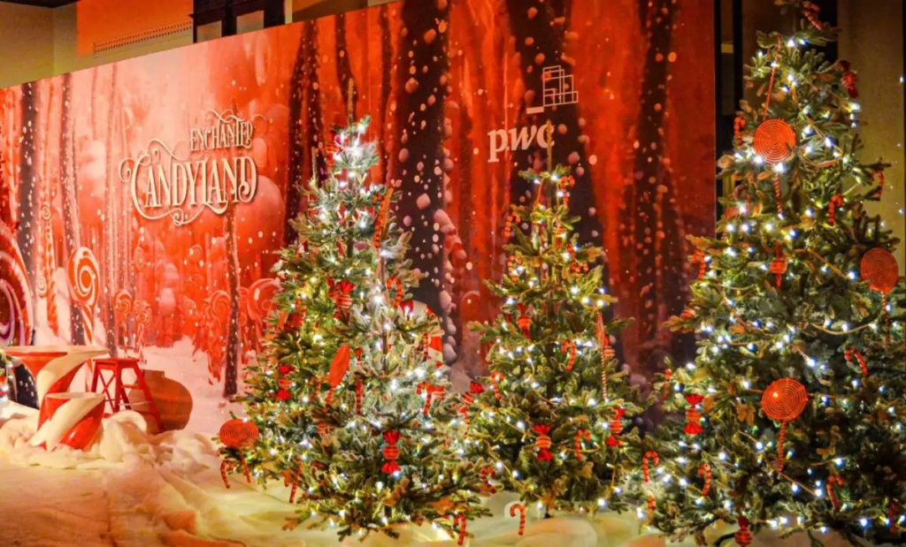 Kersttafereel met verlichte kerstbomen versierd met rode ballen en snoepgoed, achter een rode "Enchanted Candyland" decoratieve achtergrond.